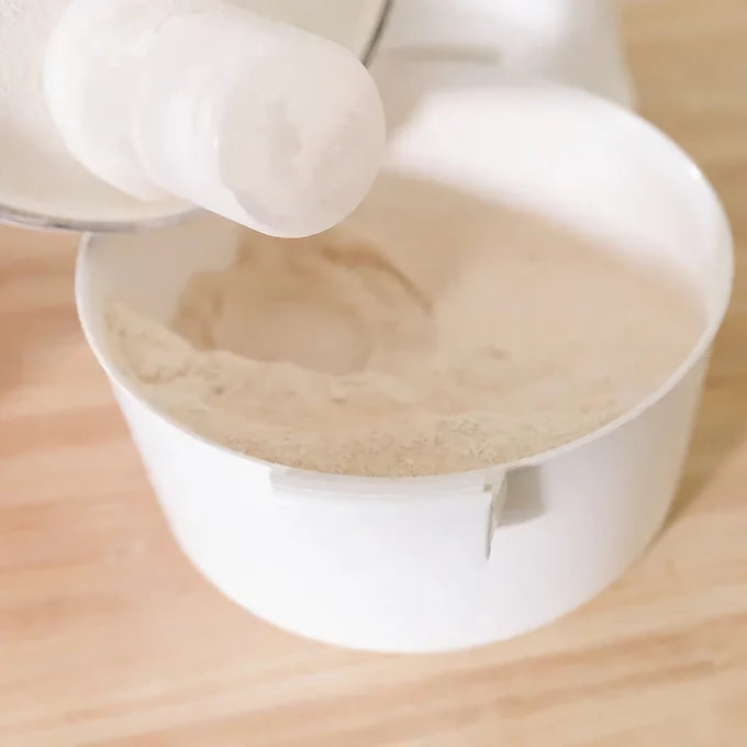 Close-up of freshly ground flour inside a white container, demonstrating fine milling from an electric grain mill, suited for Kitchen & Food, Grain Mills, and Bread Making Supplies collections.