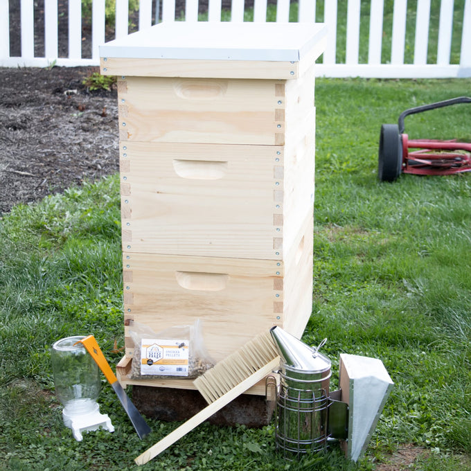 Amish-crafted natural wood 8-frame beehive with white cover and starter beekeeping tools including smoker, hive tool, bee brush, and feeder, set on grass in backyard setting for Farm, Garden & Tool and Beekeeping Supplies collections.
