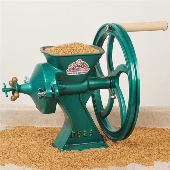 Cast iron grain mill with a green finish and wooden handle, grinding whole grains in a kitchen setting, featured in baking supplies and cookware collections.