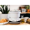 Compact white kitchen stand mixer with clear lid and adjustable dial, placed on wooden counter alongside fresh bread, olive oil, and kitchen towel, ideal for baking and kitchen helpers collections.