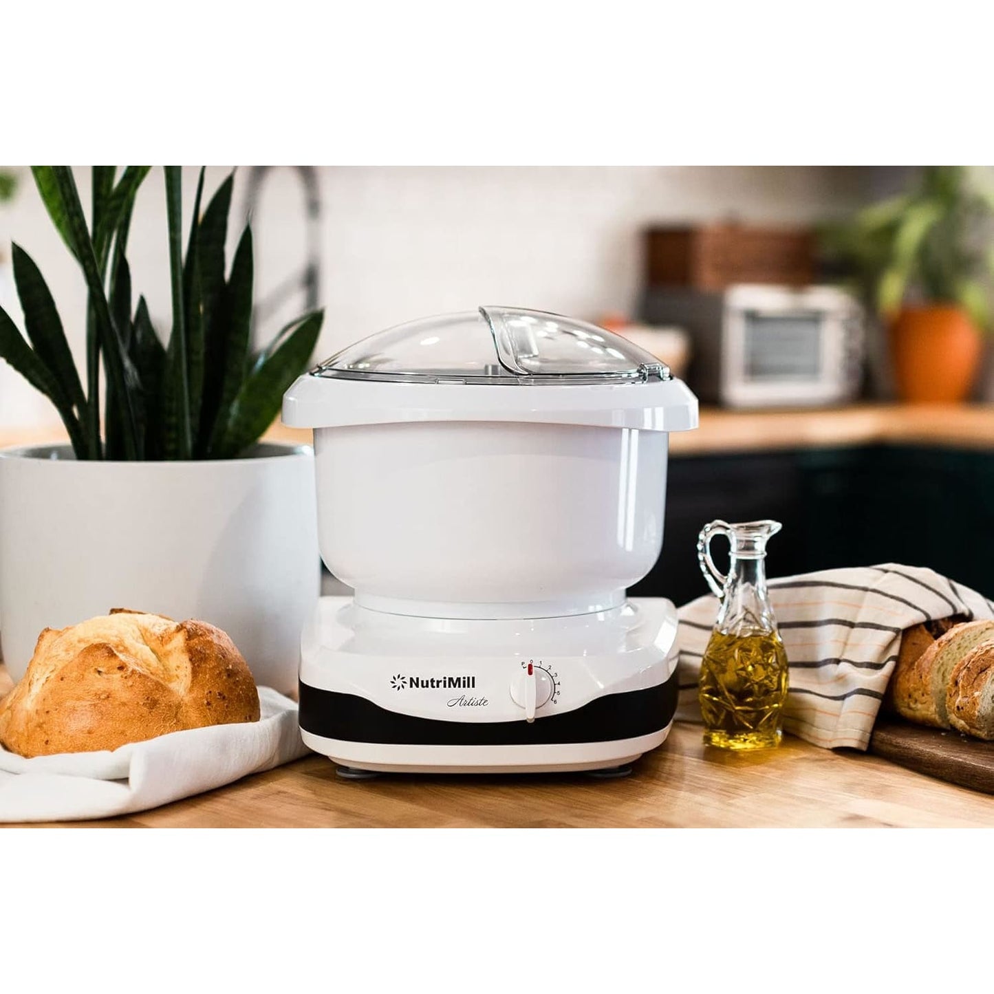 Compact white kitchen stand mixer with clear lid and adjustable dial, placed on wooden counter alongside fresh bread, olive oil, and kitchen towel, ideal for baking and kitchen helpers collections.