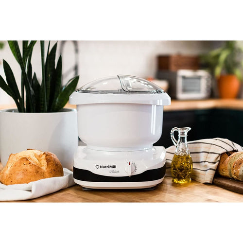 Compact white kitchen stand mixer with clear lid and adjustable dial, placed on wooden counter alongside fresh bread, olive oil, and kitchen towel, ideal for baking and kitchen helpers collections.
