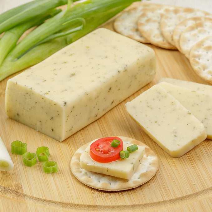 Handcrafted shelf-stable cheese block with herb flecks, sliced and served on crackers with green onions and a tomato slice, ideal for Kitchen & Food, Pantry, Snacks and Sweets, USA Made, Best Sellers, and Promo Eligible collections.